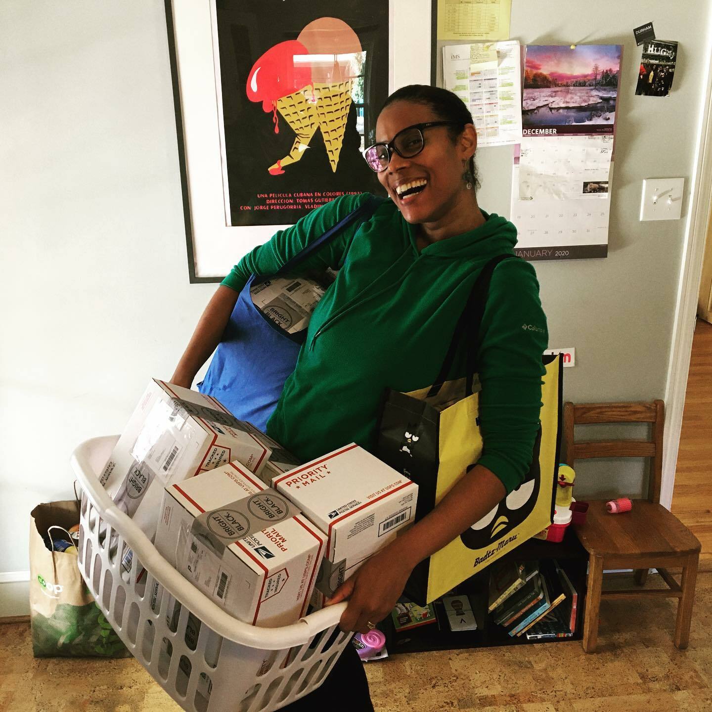 A woman smiling and carrying a laundry basket overflowing with packages to ship out. 